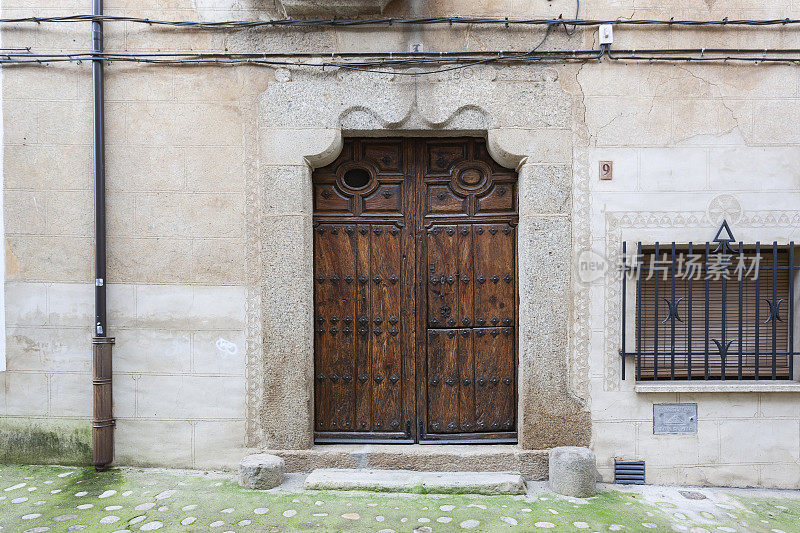 埃斯特雷马杜拉卡塞雷斯的维拉纽瓦(Villanueva de la Vera)镇，一所房子的入口处有一扇古老的雕花木门，上面装饰着铁饰品。